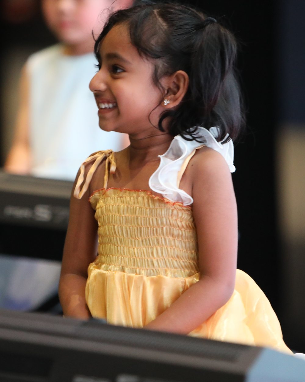 Ghoshi smiling at the piano in a yellow dress